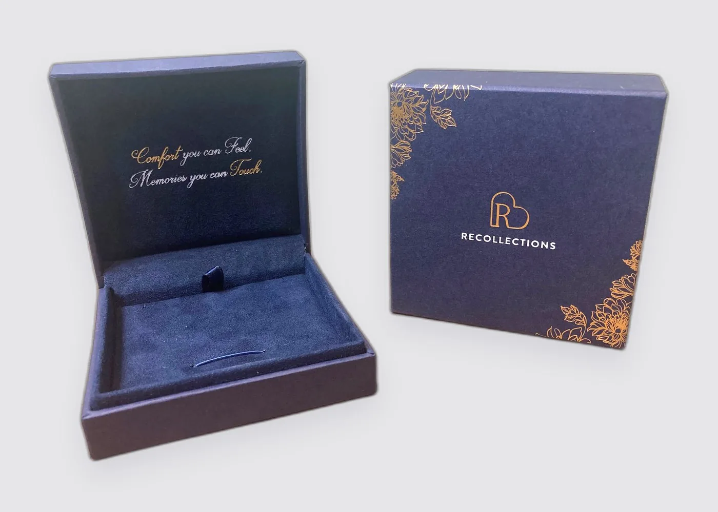 The navy presentation box open, showing the velvet interior and the words
                &ldquo;Comfort you can Feel, Memories you can Touch&rdquo; printed inside the lid,
                beside the closed outer box, navy with the Recollections mark and a gold
                botanical border